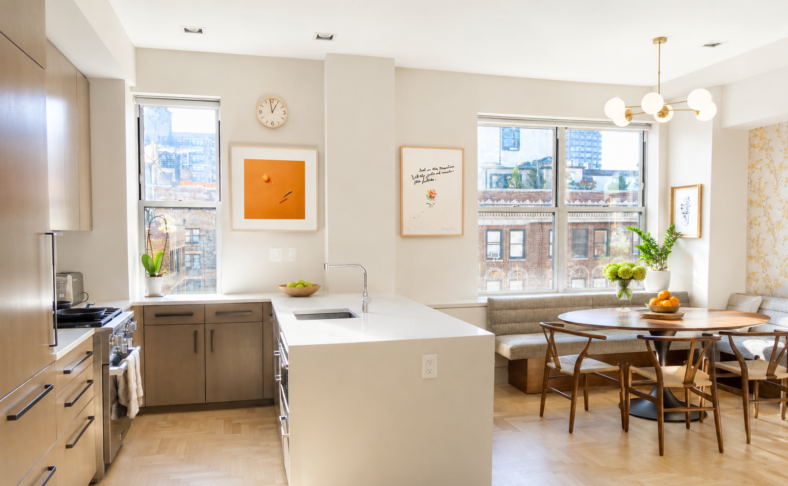 Same kitchen + dining after editing — neutral whites, countertop clutter cleared, intentional staging (plants, fruit bowl, flowers, art) preserved, layout and finishes unchanged.